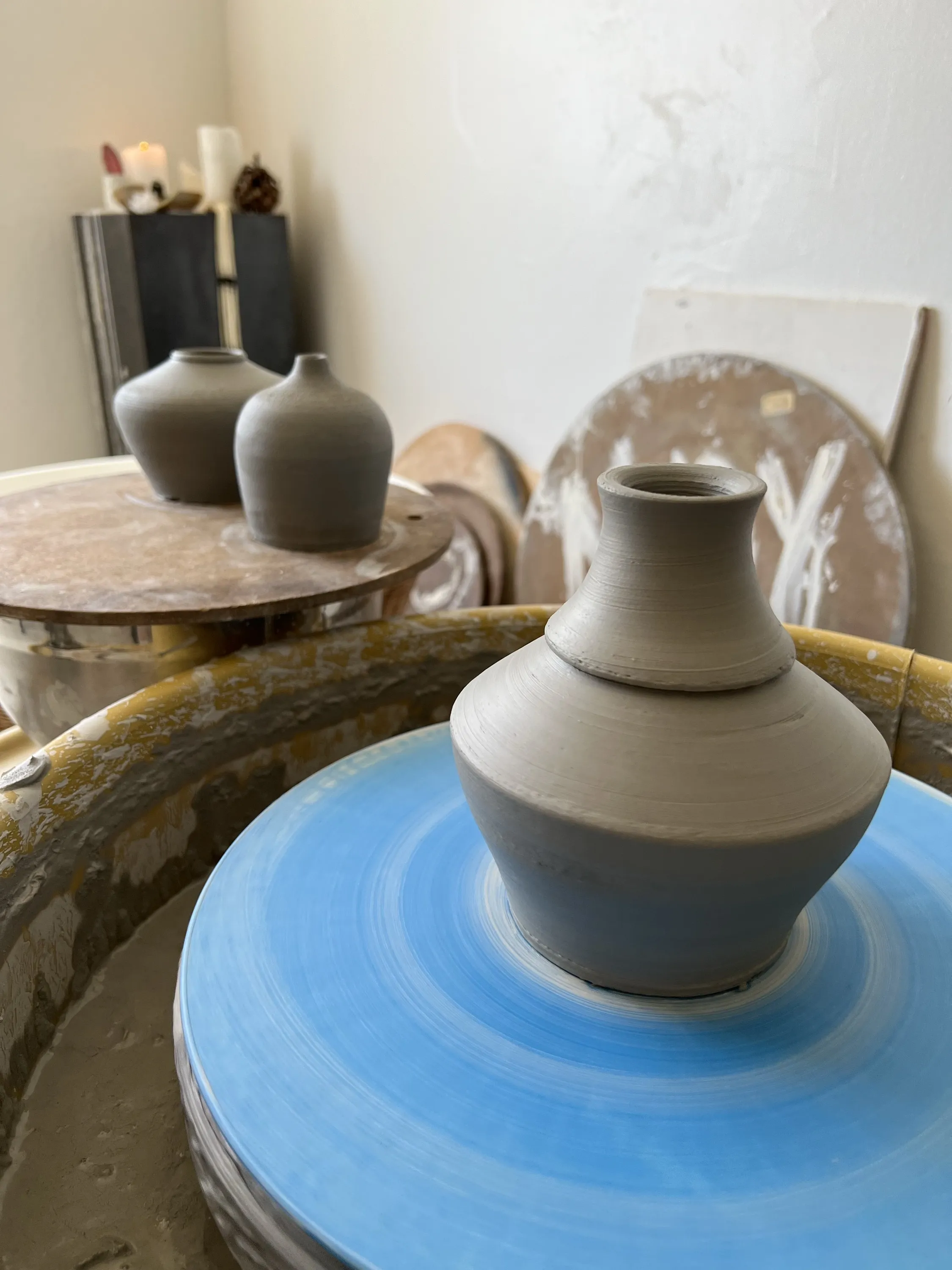 Freshly thrown vase on the wheel with greenware drying behind